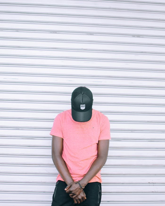A casual portrait of a man wearing a pink shirt and cap against a striped background.